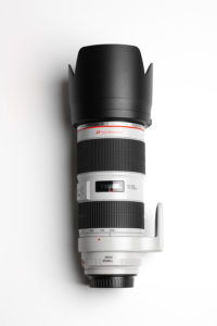 - Location de Studio équipé pour la Photo et la Vidéo Un objectif de caméra blanc avec un anneau de mise au point en caoutchouc noir et un pare-soleil. Il possède des marques de zoom allant de 70 à 200 mm et un stabilisateur d'image. Le logo ULTRASONIC est visible, indiquant une mise au point rapide. L'objectif est placé debout.