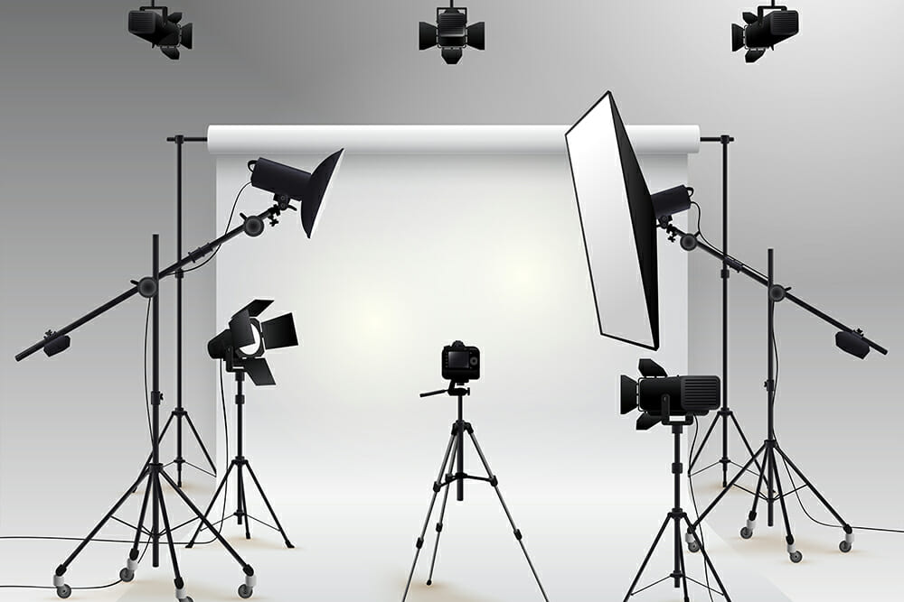 - Location de Studio équipé pour la Photo et la Vidéo Un studio photo professionnel avec des trépieds, des appareils photo, des éclairages et des diffuseurs autour d'un fond blanc. Des lumières au plafond ajoutent de la clarté pour bien éclairer les séances photo.
