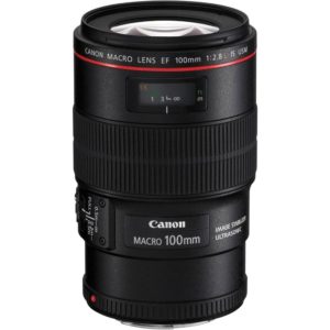 - Location de Studio équipé pour la Photo et la Vidéo L'objectif Canon Macro EF 100mm f/2.8L IS USM est posé debout. Il est doté d'un stabilisateur d'image et d'un moteur ultrasonique, avec des marqueurs de distance visibles. L'objectif est principalement noir avec des accents rouges.